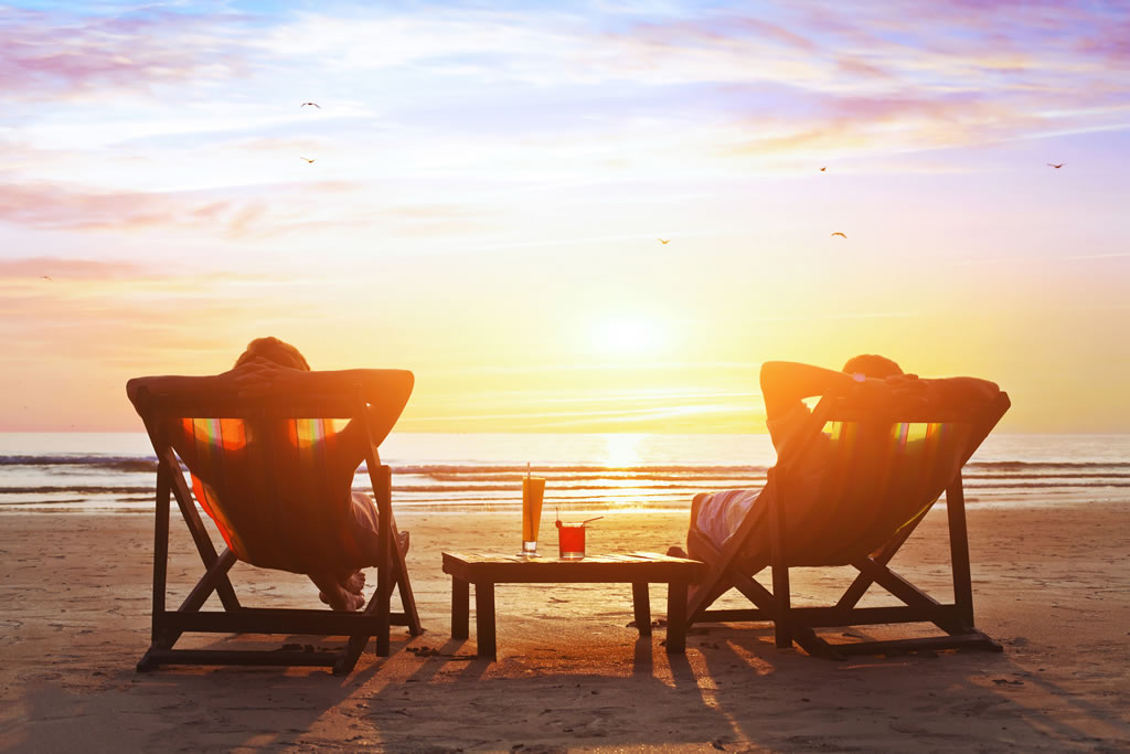 Couple relaxing on beach at sunset with drinks.